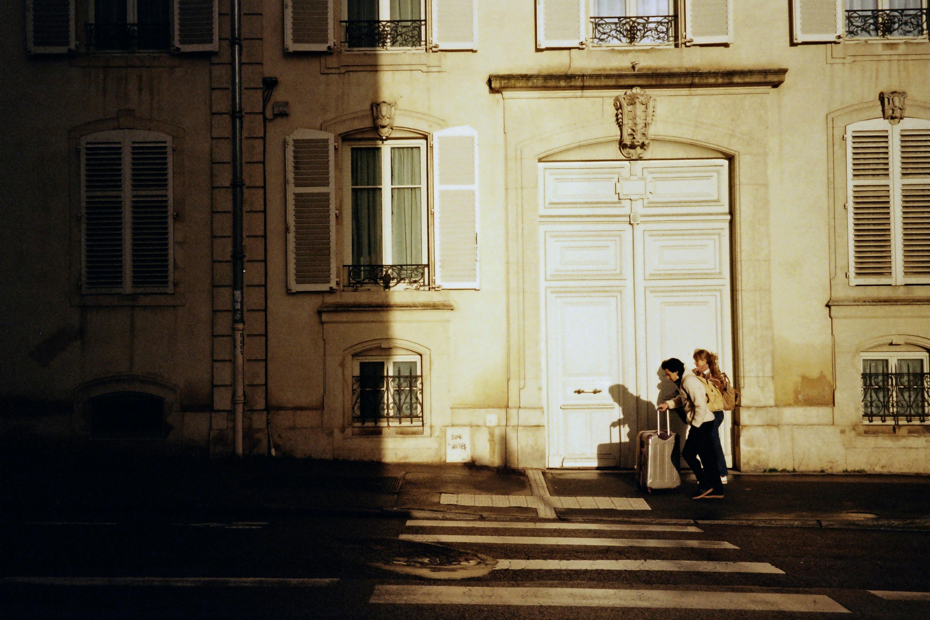 Two people walking past a historic building in Nancy, France, during sunrise.
