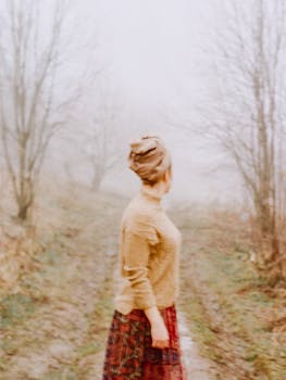 秋日，一名女子沿着雾气弥漫、树木光秃的小路行走，营造出一种宁静而神秘的氛围