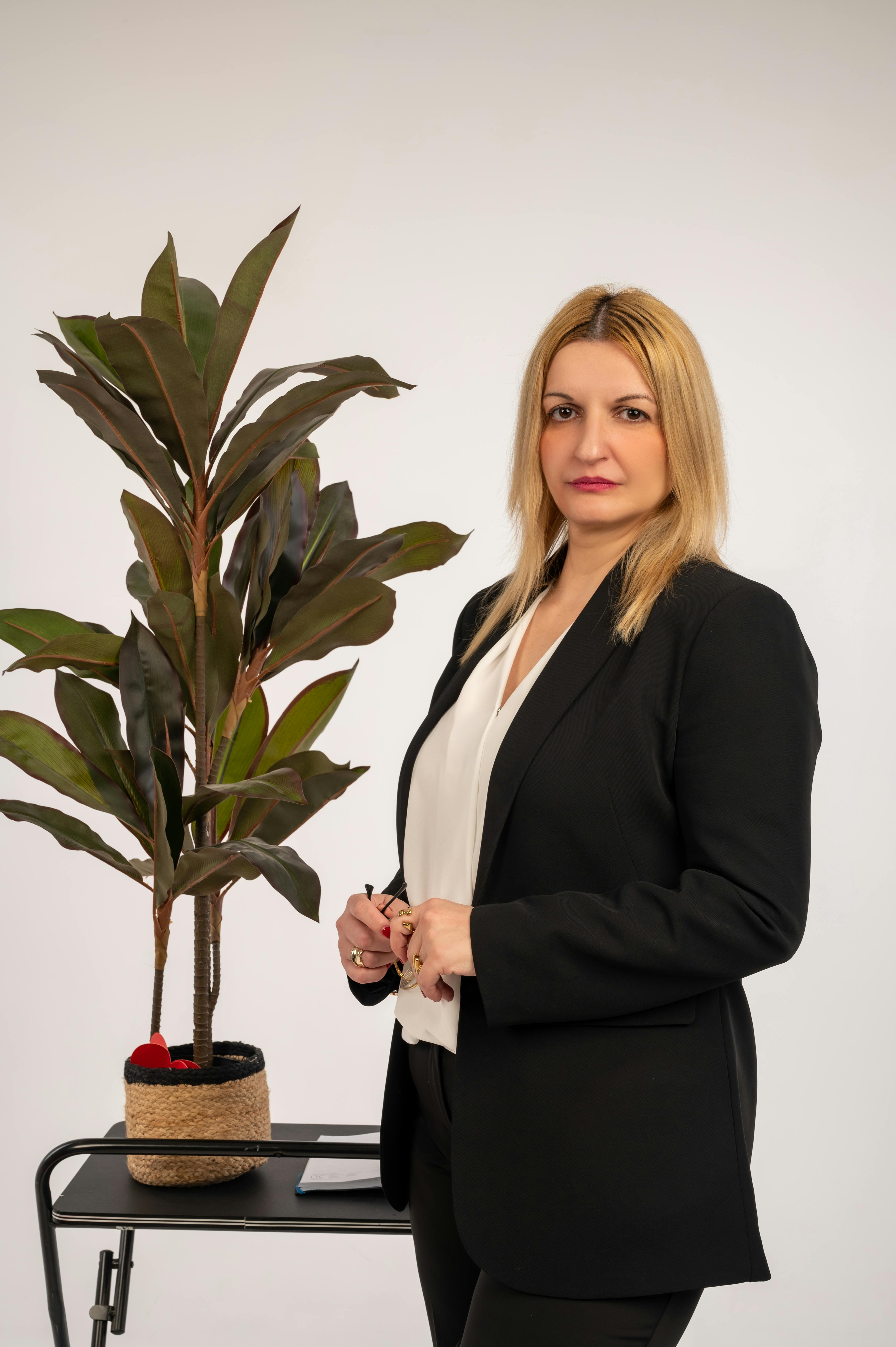 Professional woman in a business suit standing beside an indoor plant, showcasing a modern office setting.