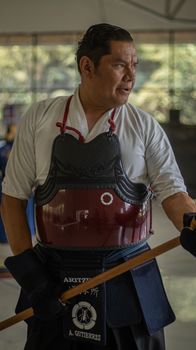 A person practicing Kendo in a dojo, wearing traditional armor and holding a bamboo sword.