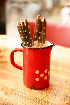 A red jug with polka dots holding various cutlery on a wooden table.