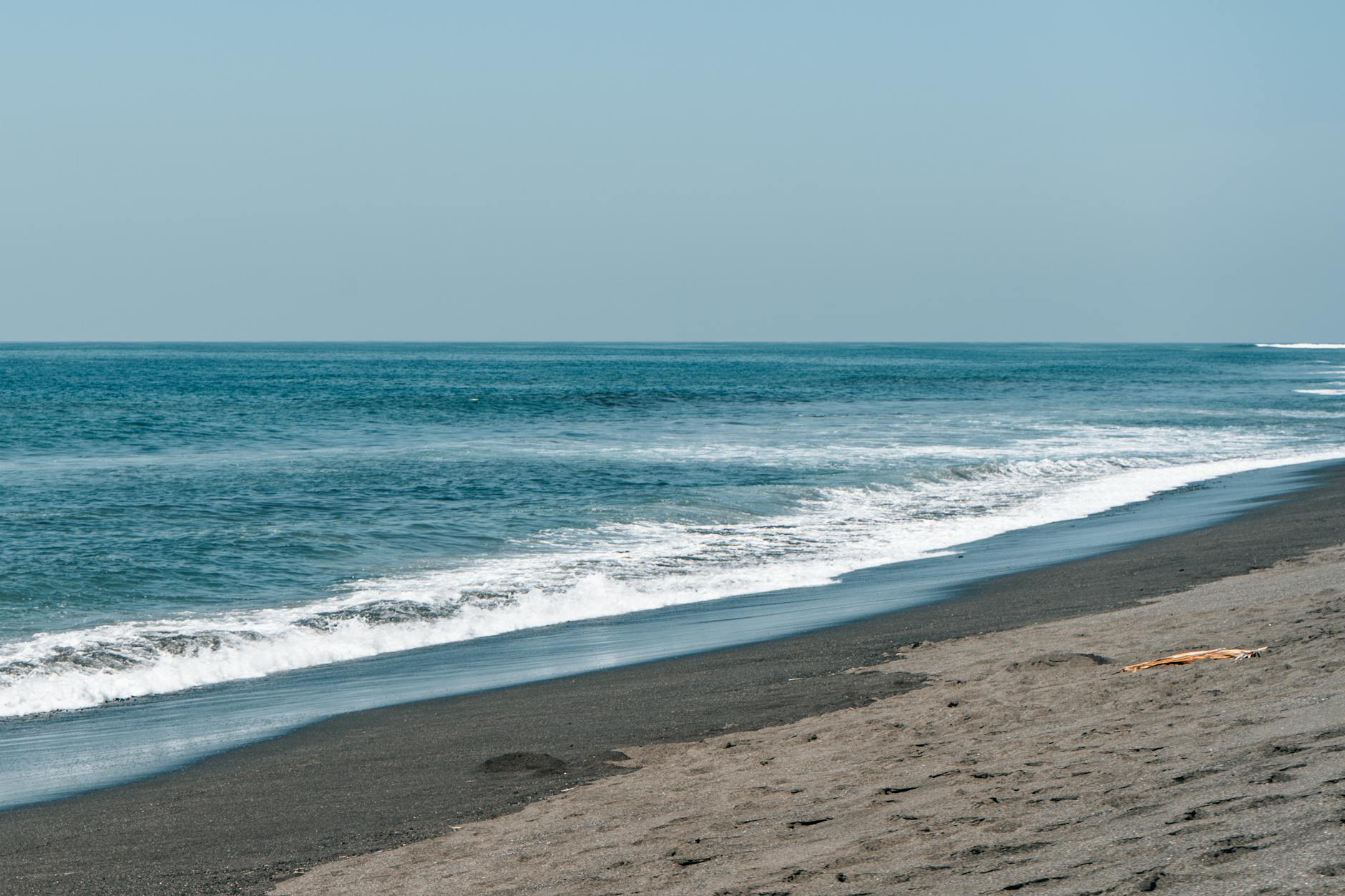 A tranquil sandy beach with gentle ocean waves under clear blue skies, perfect for a peaceful escape.
