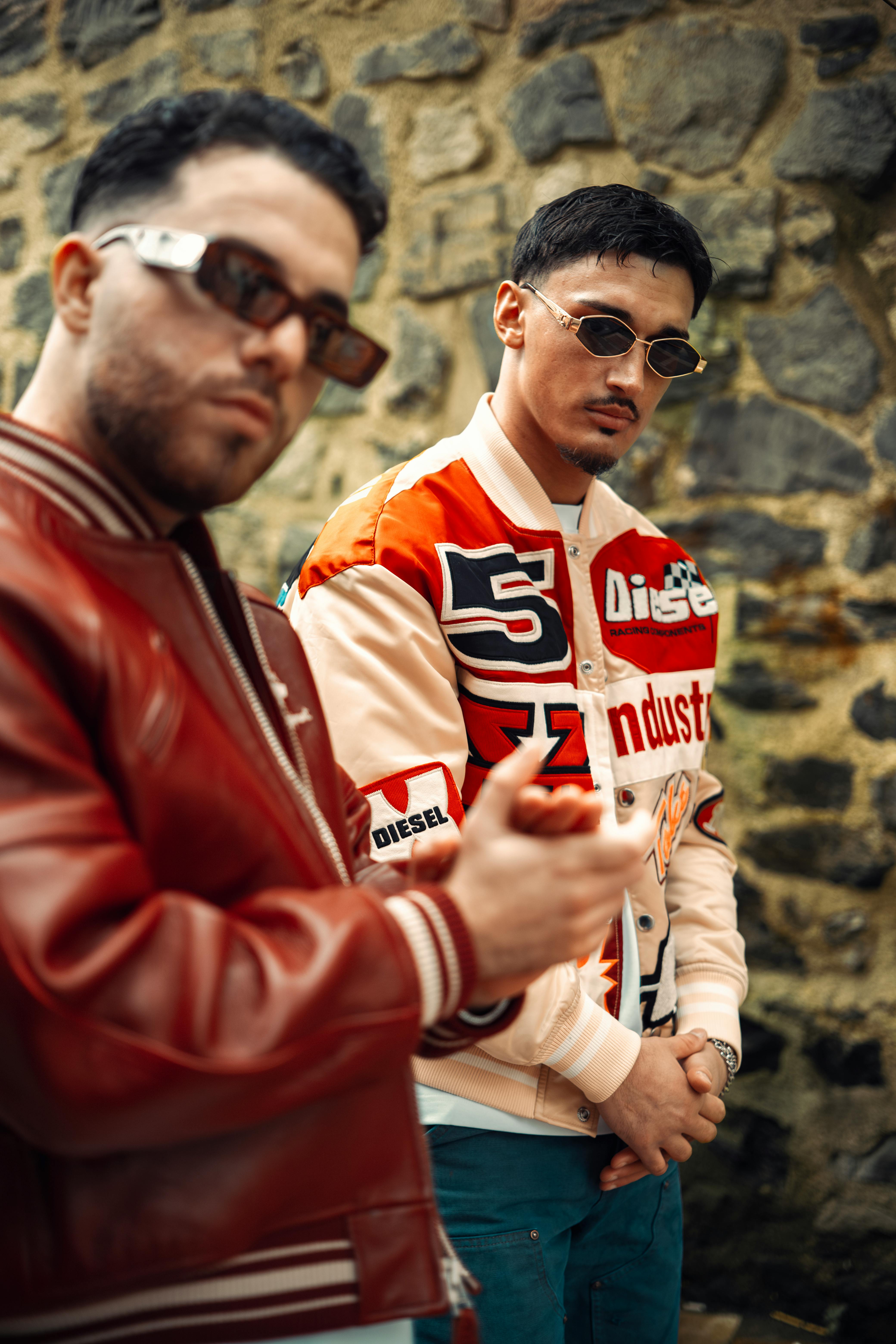 Two stylish men posing in trendy street fashion with sunglasses outdoors.