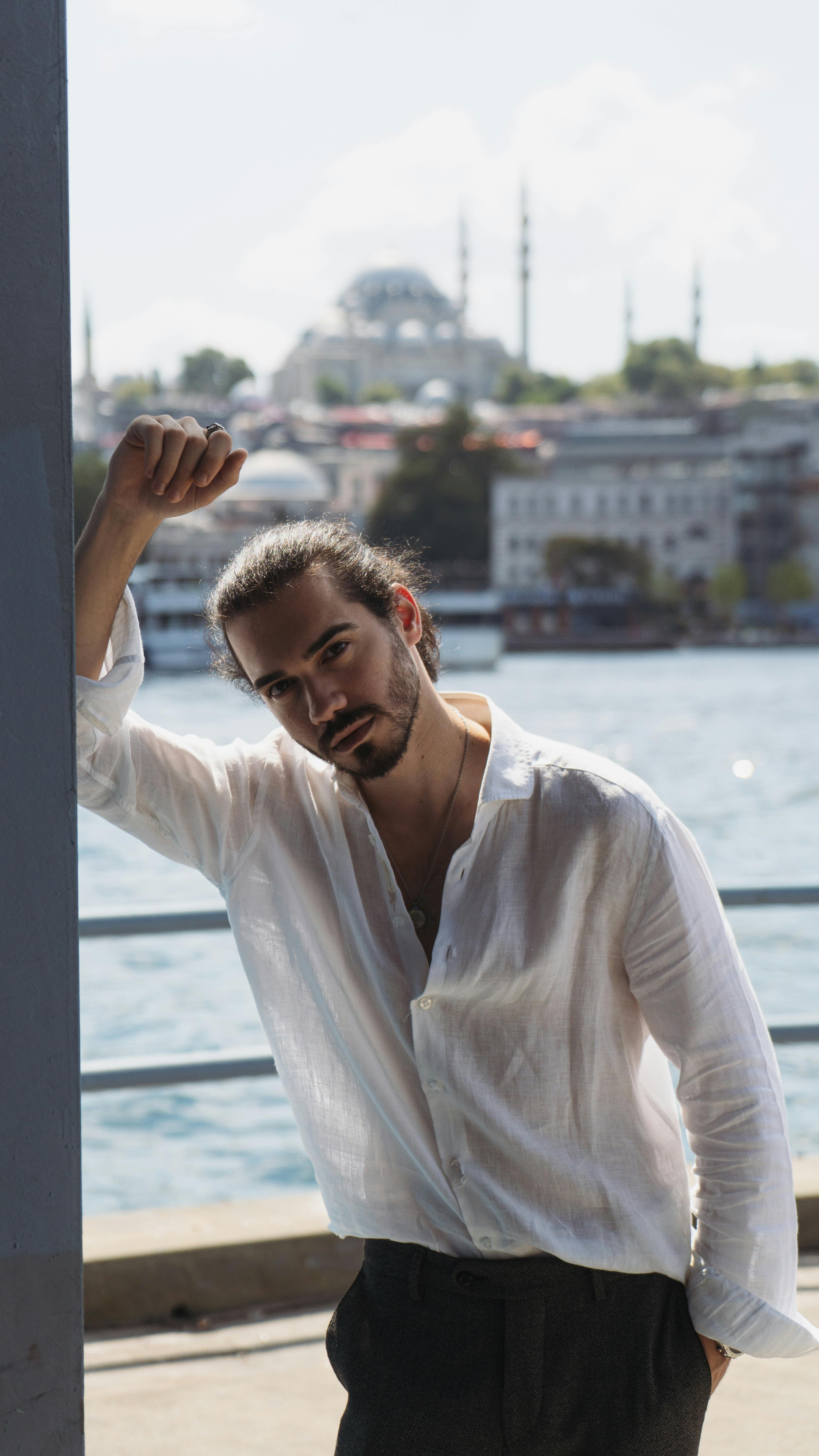 Young man in casual white shirt posing by the Bosphorus with cityscape background.