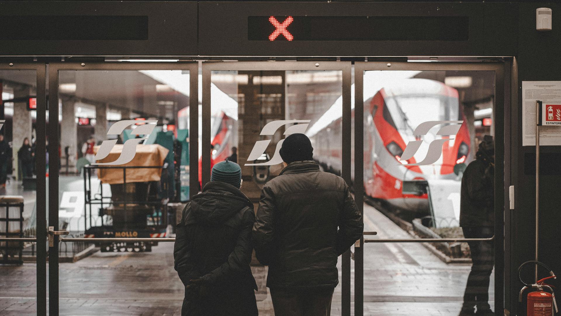 Two people standing at Florence train station entrance, looking at train.