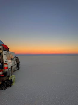 A traveler beside a vehicle at sunset on the vast Salar de Uyuni salt flats in Bolivia.