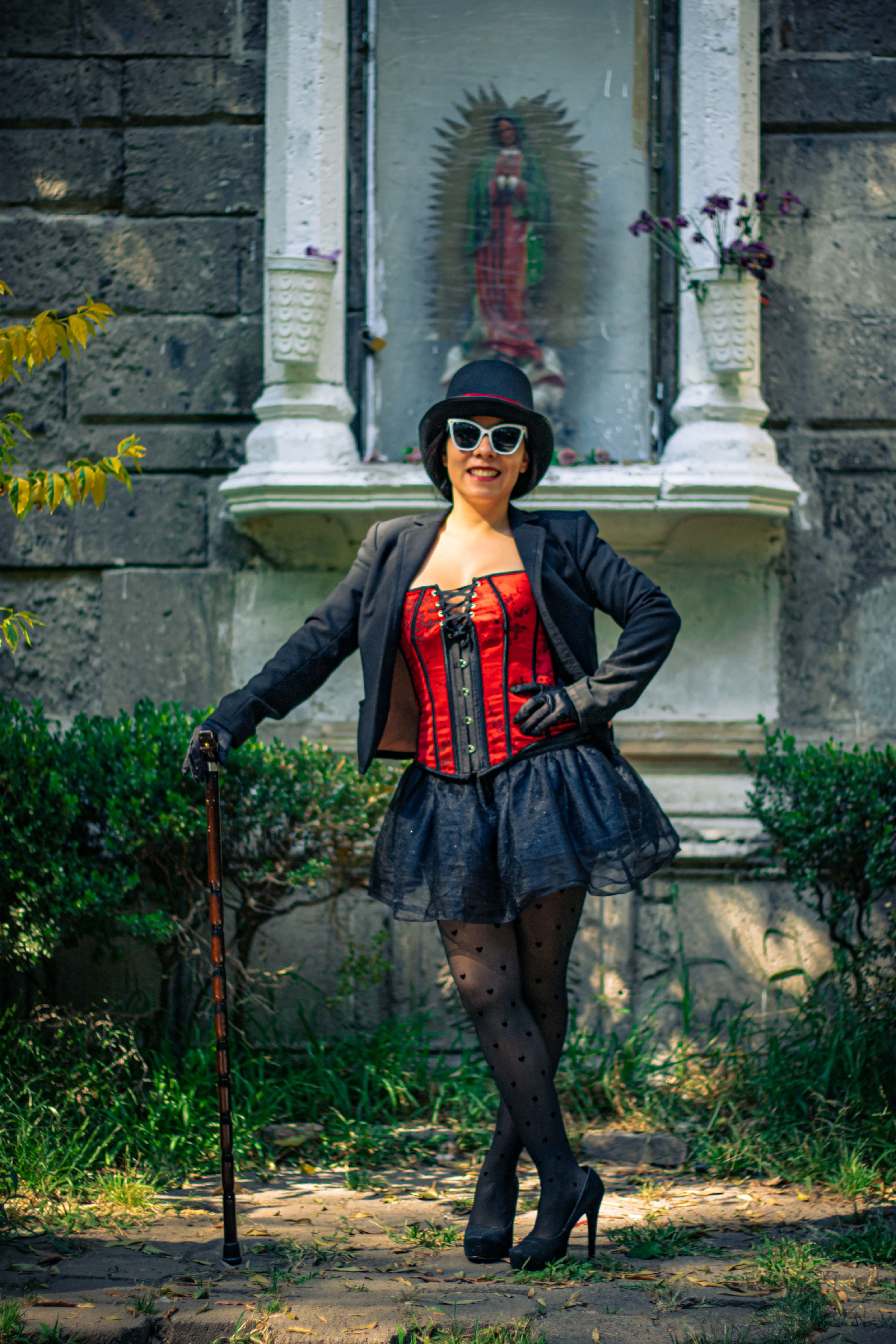 Chic woman in red corset and hat posing in park with a statue backdrop