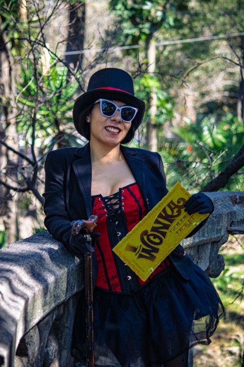 Free Chic woman in a park wearing a red corset, black skirt, and hat, holding a Wonka ticket. Stock Photo