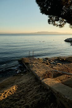 Serene beach scene with stone stairs leading to a calm seascape under a sunset sky.