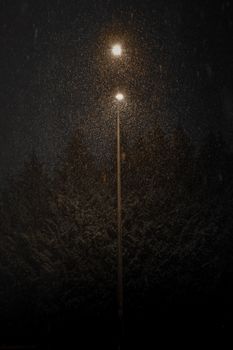 A streetlamp shines through falling snowflakes, creating a serene winter night atmosphere.