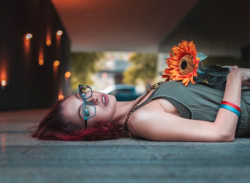 Free A fashionable woman with glasses holding a sunflower, lying outside in a stylish pose. Stock Photo