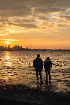Serene sunset over Istanbul's waterfront with two people and seagulls in silhouette.
