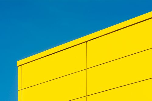 Free Minimalist image of a vibrant yellow building facade contrasted with a clear blue sky. Stock Photo