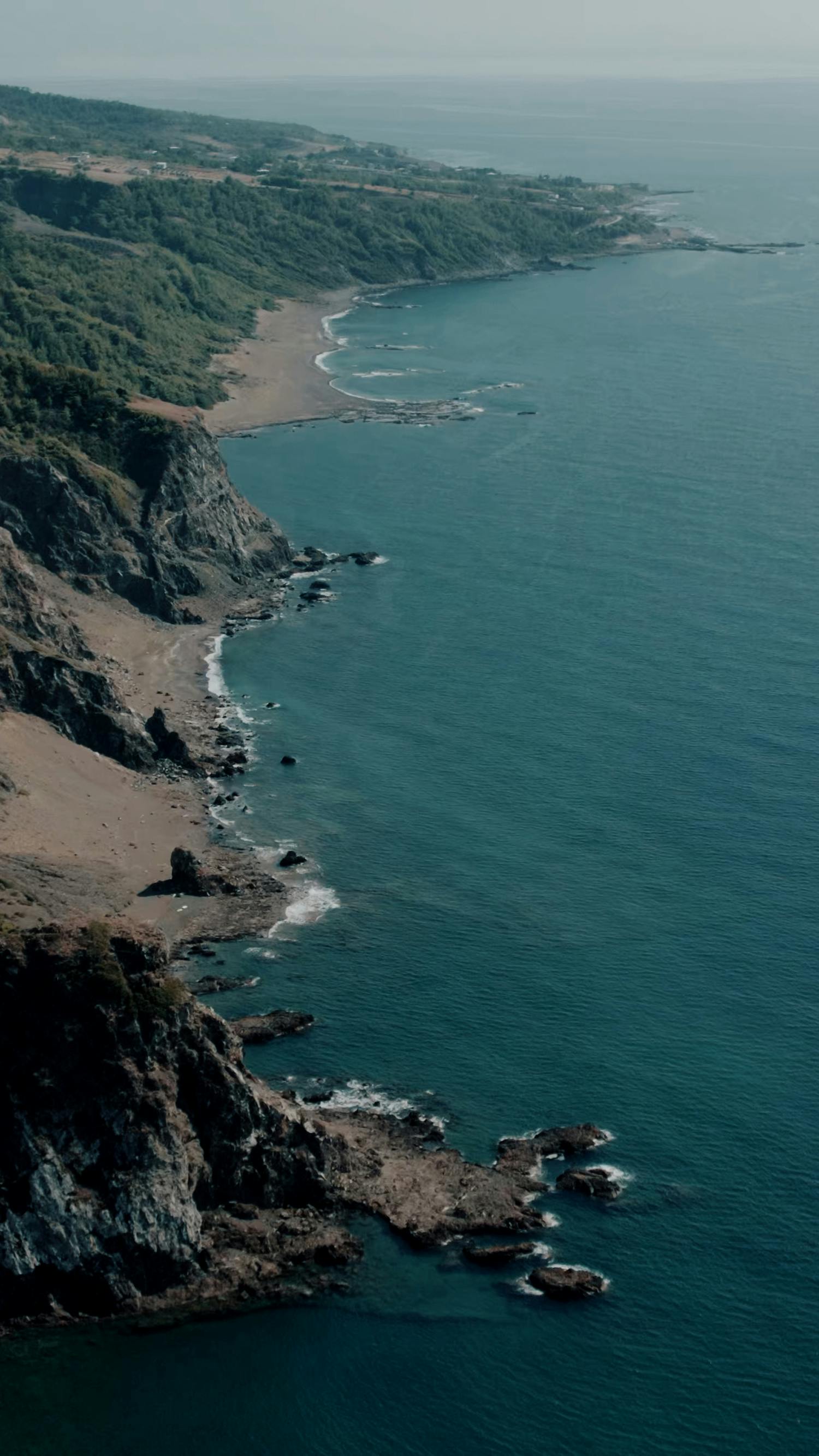 A breathtaking aerial view of the rugged Hatay coastline with cliffs and deep blue sea.