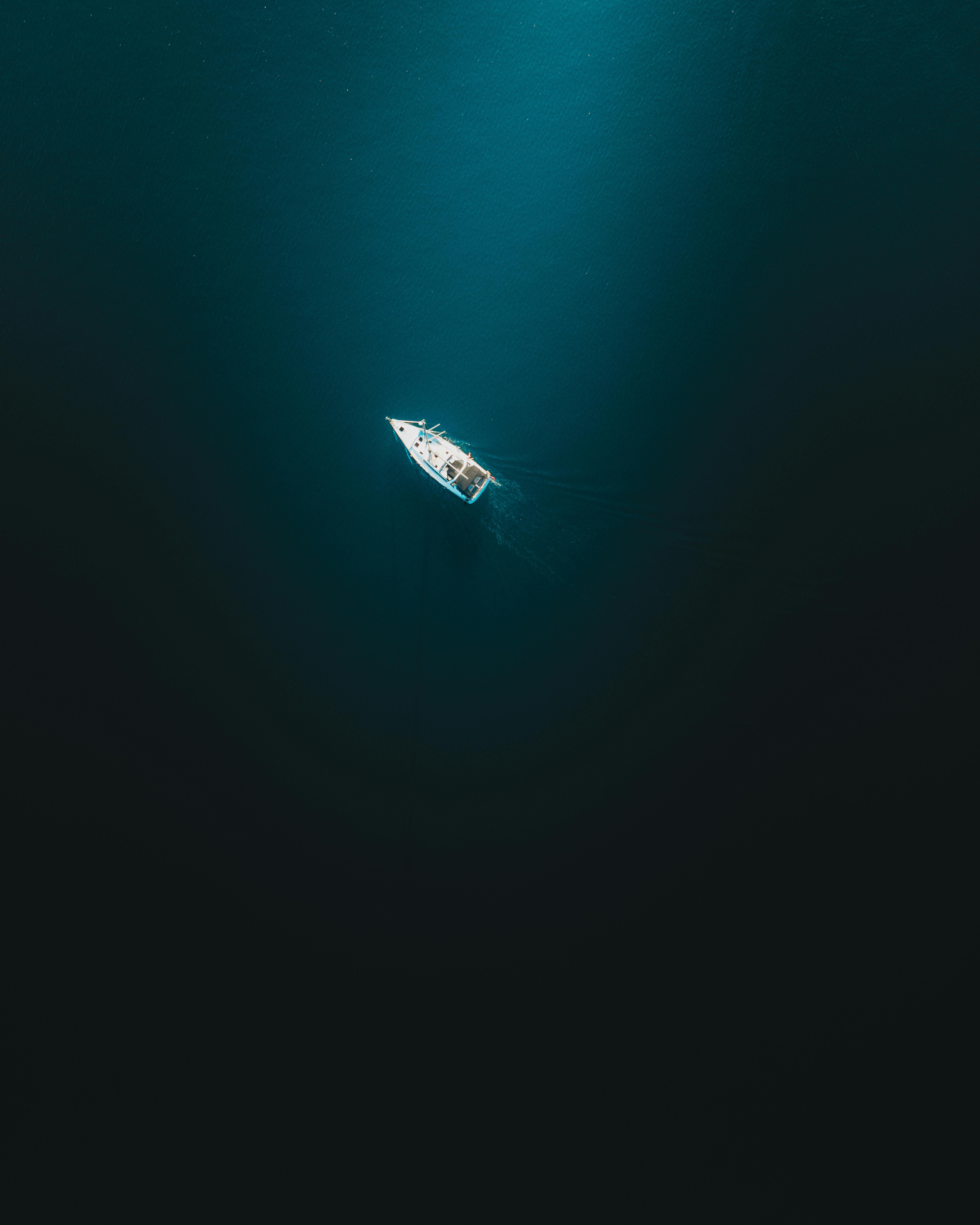 A solitary boat sails over the deep blue ocean, captured from above, evoking a sense of serenity and adventure.