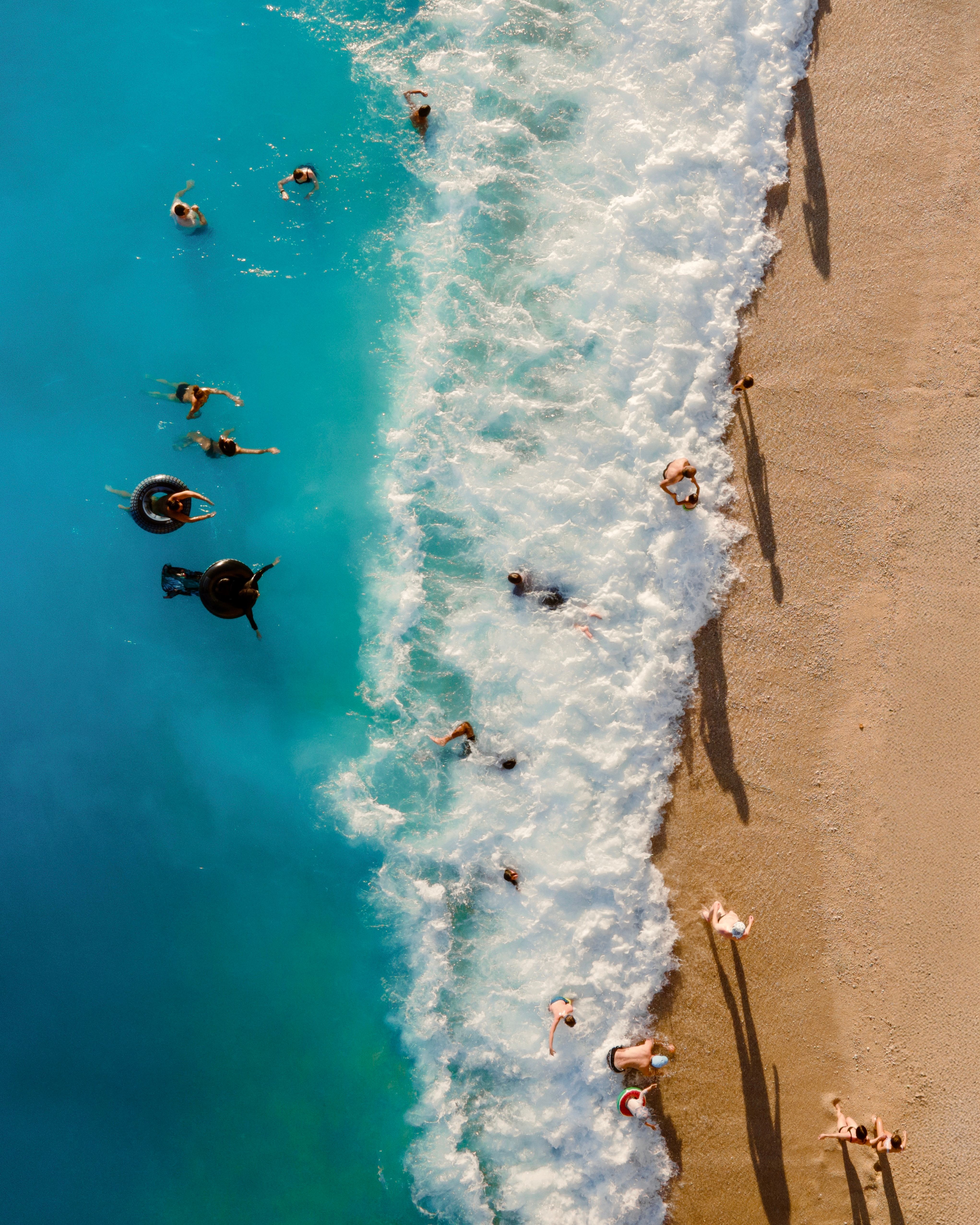 Aerial shot of people swimming and relaxing on a sunny beach with blue ocean waves.
