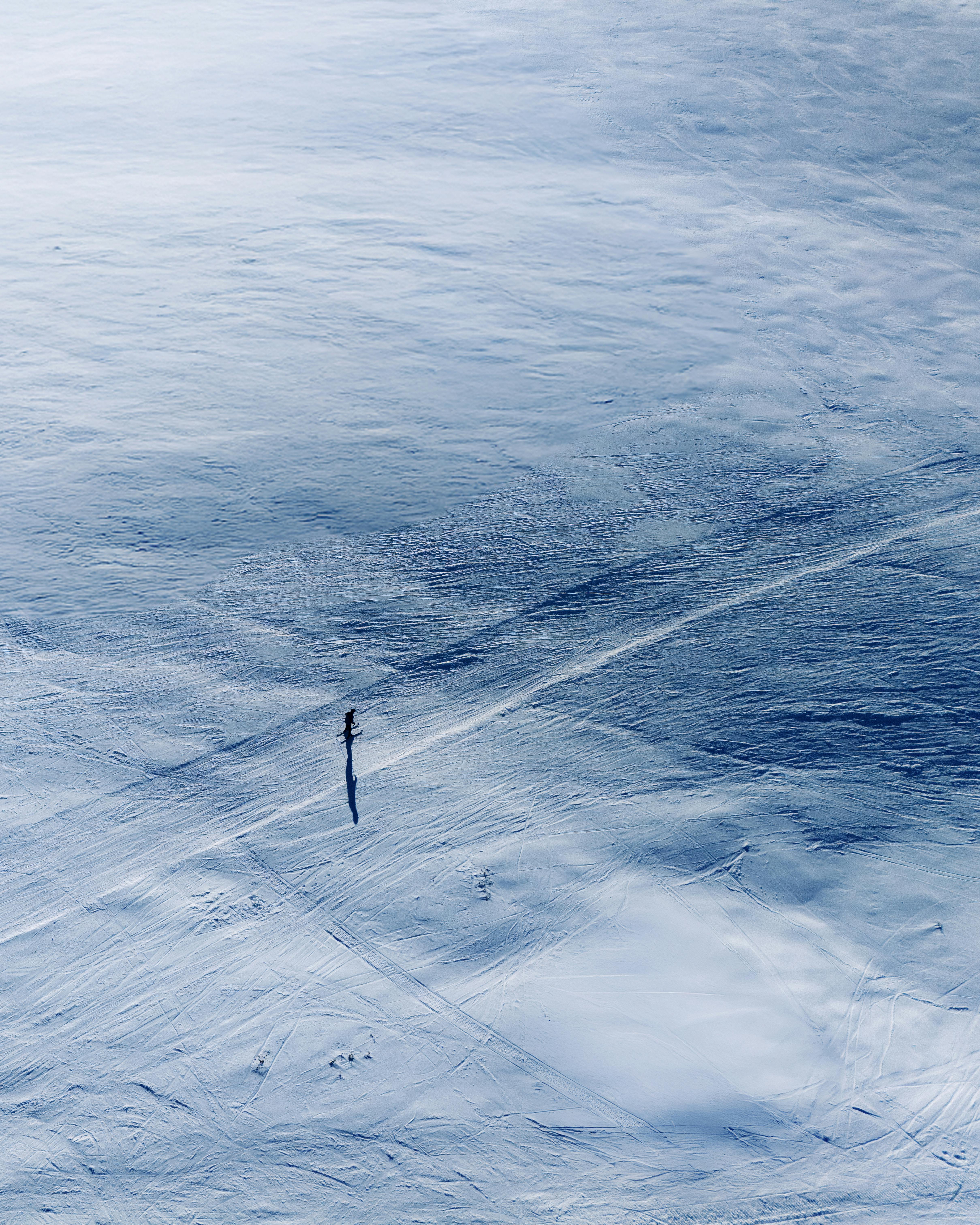 A solitary skier traverses a vast snowy landscape, captured from above offering serene winter solitude.