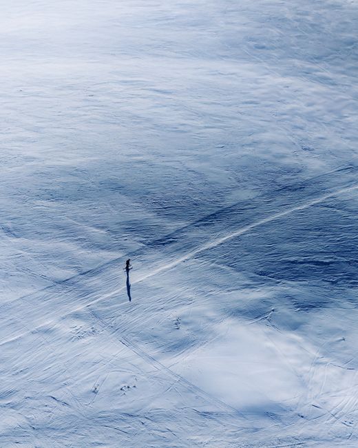 A solitary skier traverses a vast snowy landscape, captured from above offering serene winter solitude.
