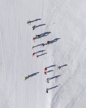 Aerial shot of skiers on a snowy slope casting long shadows, with bright ski apparel.
