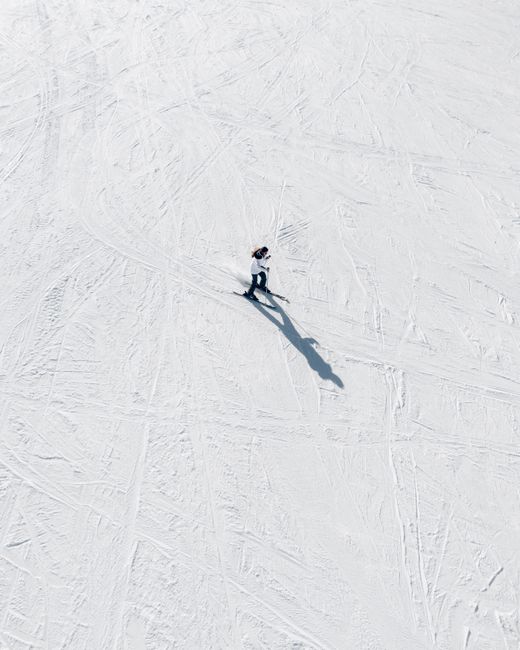 Aerial view of a solitary person snowboarding down a wide, snowy slope under clear skies.