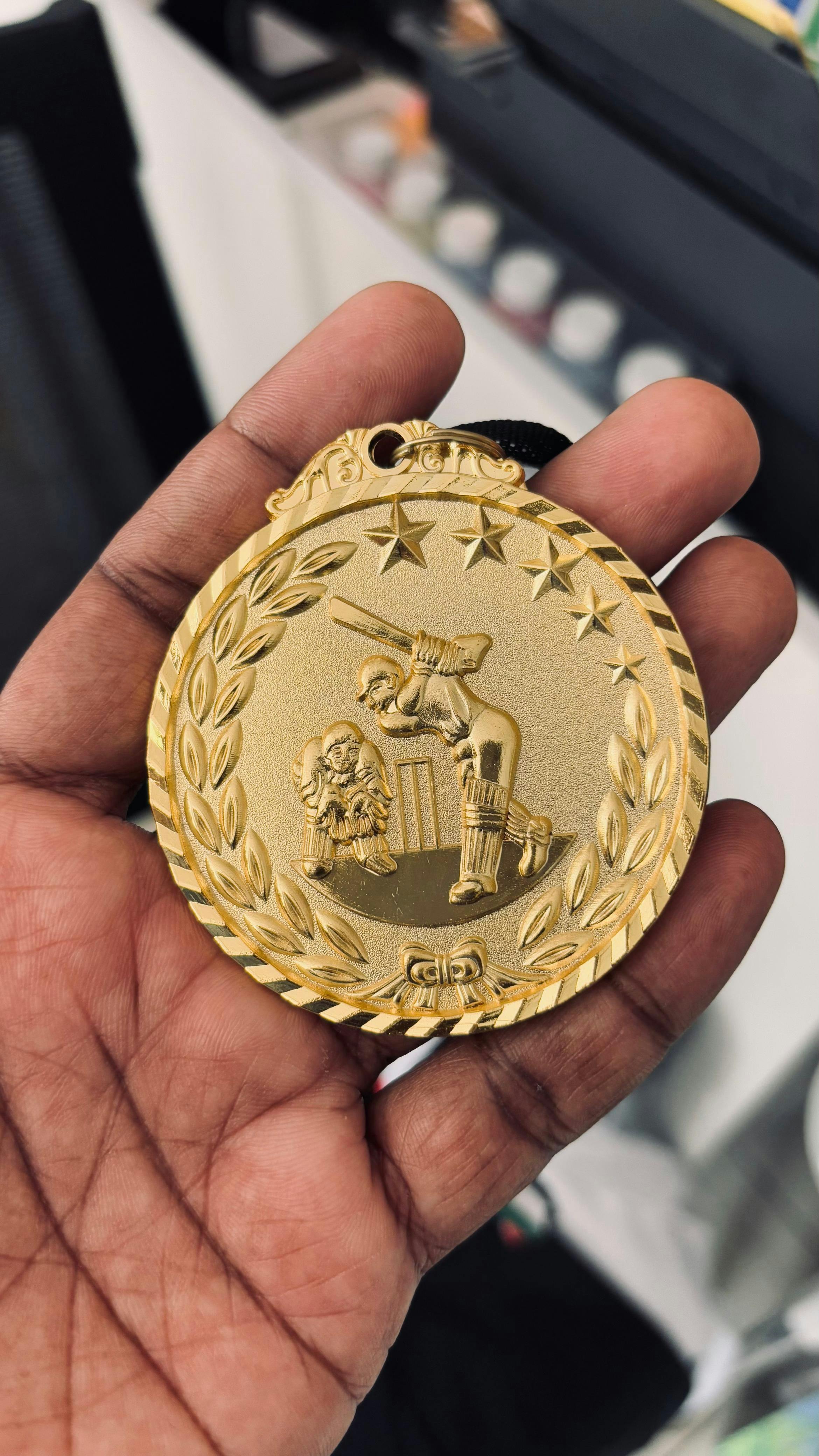 gold cricket medal held in hand close up