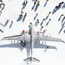 An aerial, top-down view of large military drones on display, surrounded by people casting long shadows on the white ground.