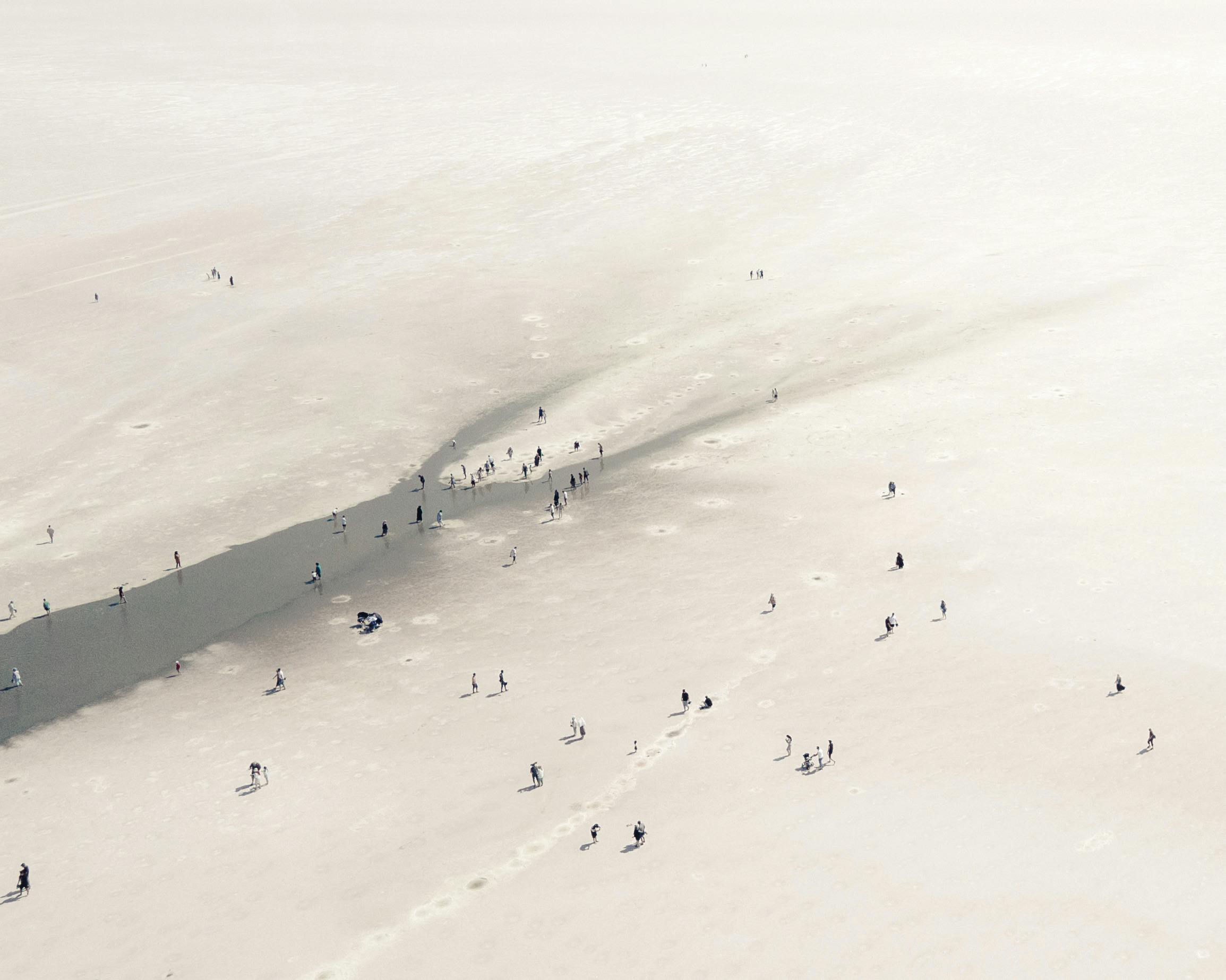 Aerial shot capturing people strolling on a vast sandy area, creating a unique and abstract scene.