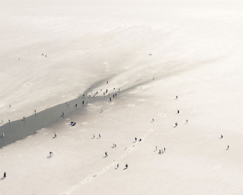 Aerial shot capturing people strolling on a vast sandy area, creating a unique and abstract scene.