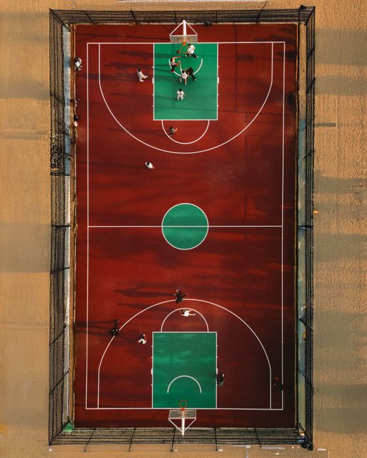 Top-down view of a basketball game on an outdoor court at sunset.