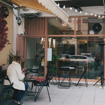 Une scène paisible à l'extérieur d'un café élégant avec une personne assise, idéale pour une ambiance urbaine détendue.
