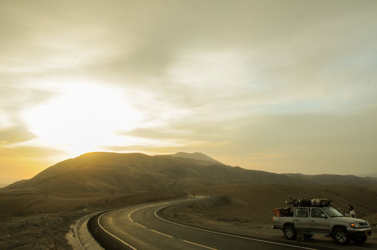 A breathtaking road trip scene in Peru, showcasing a winding road and a tranquil sunset over mountains.