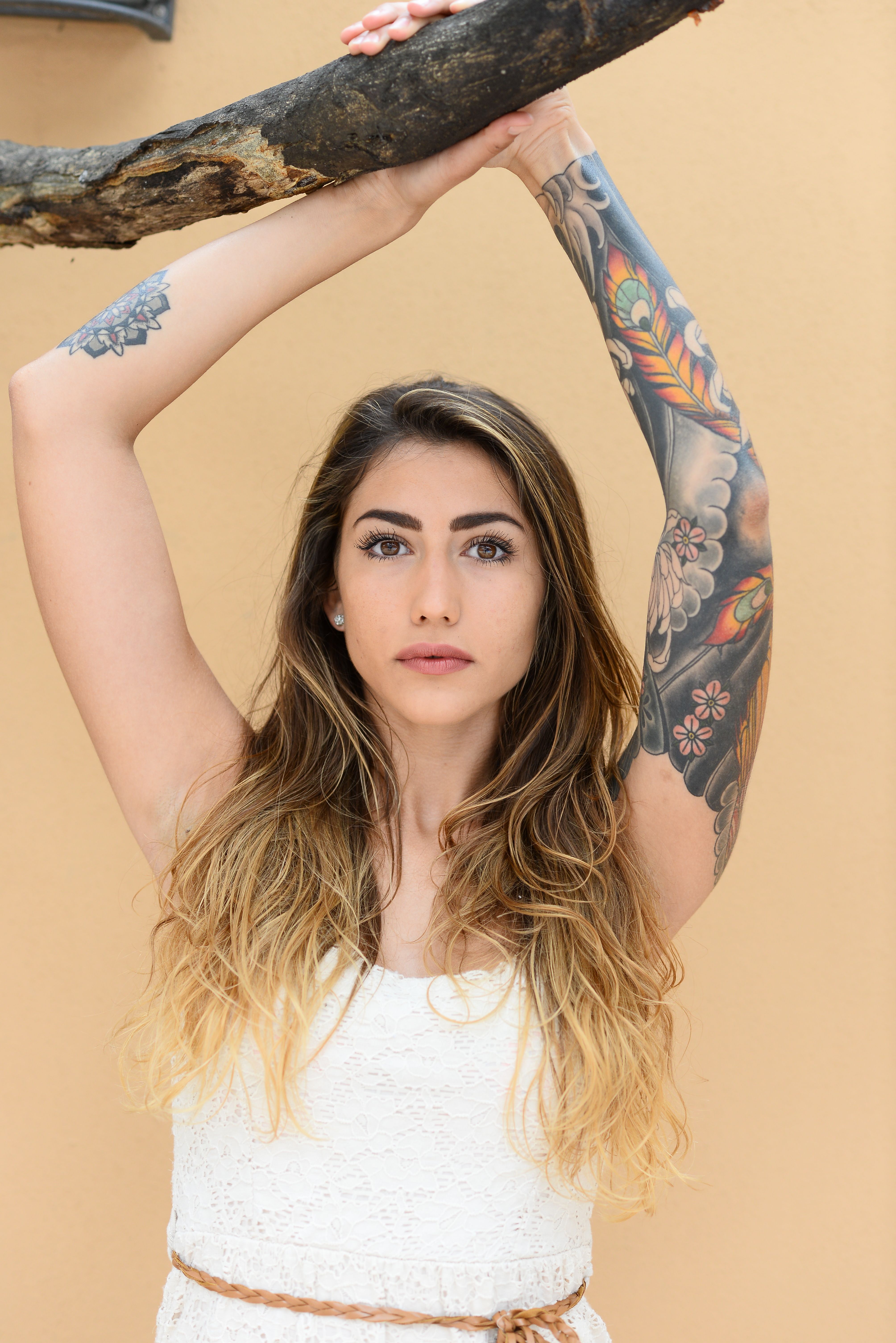 Young woman with vibrant tattoos posing against a warm-toned wall, showcasing her unique style.
