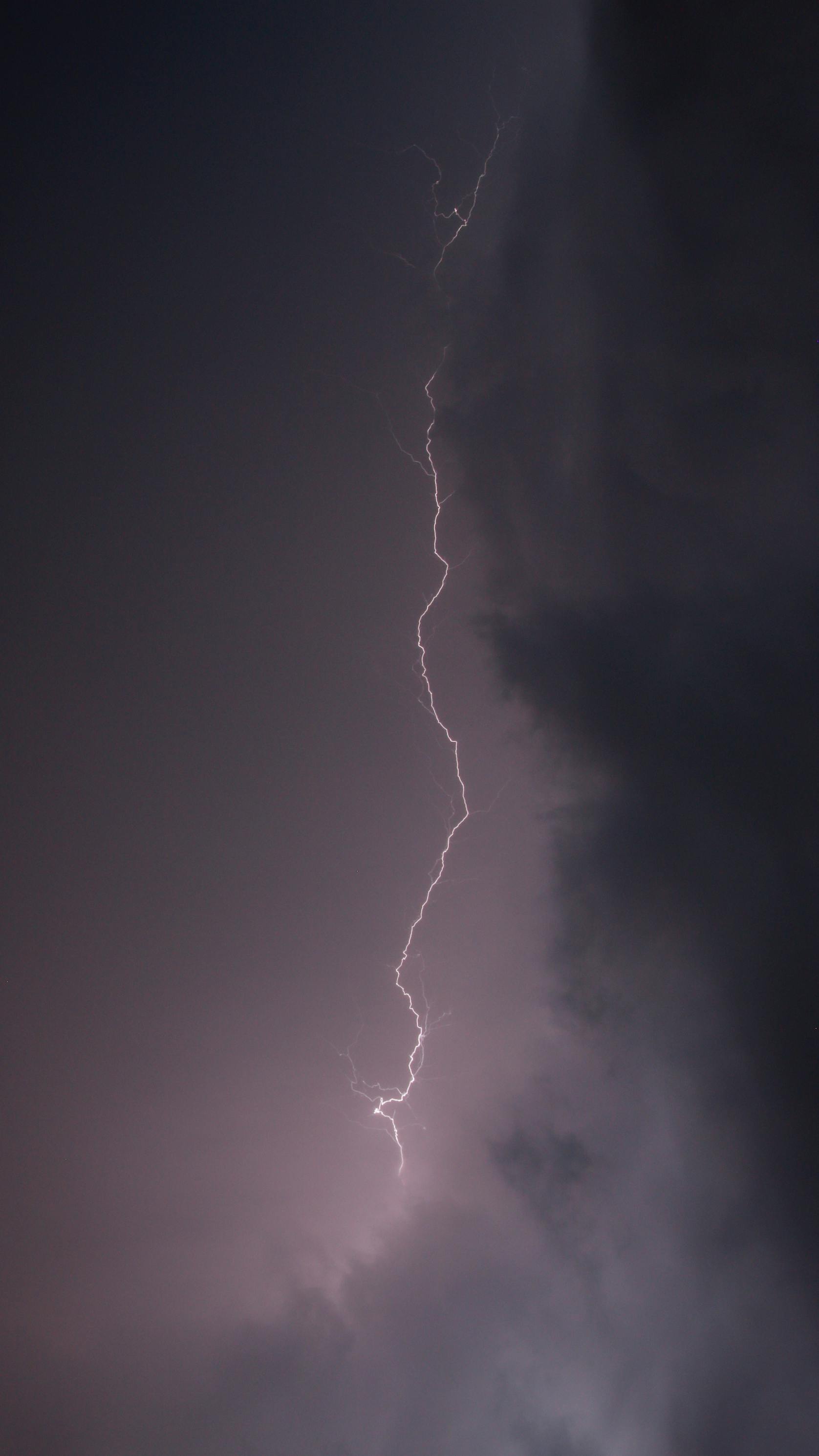 A striking lightning bolt descends from dark storm clouds, illuminating the night sky.
