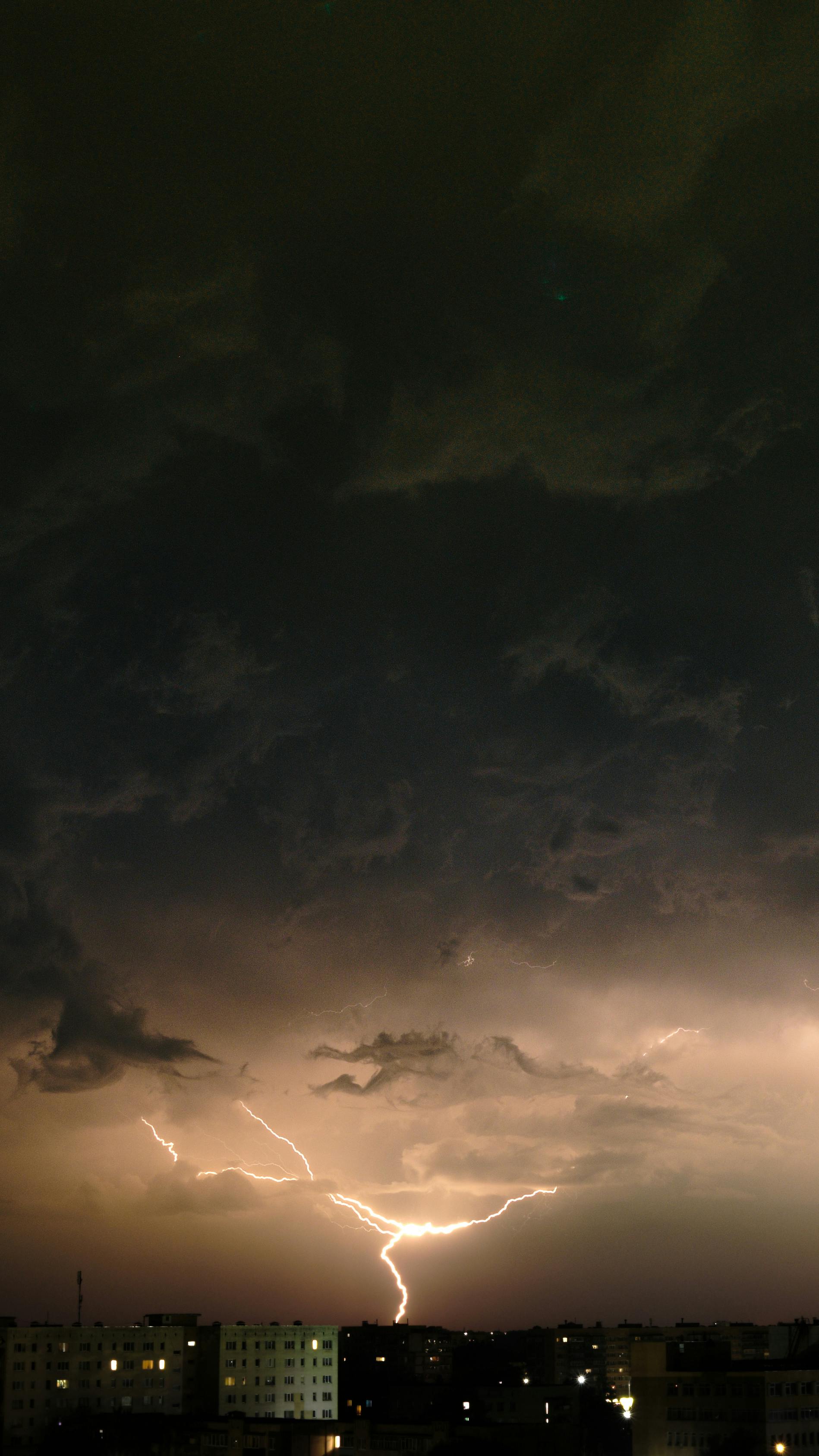 A striking lightning bolt illuminates a cityscape under dark stormy clouds at night.