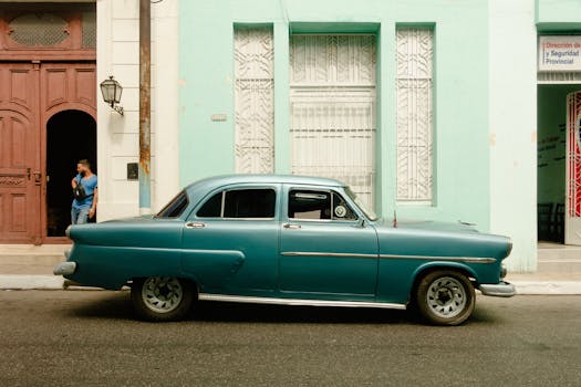 Classic blue car on a vibrant Cuban street with architectural details.