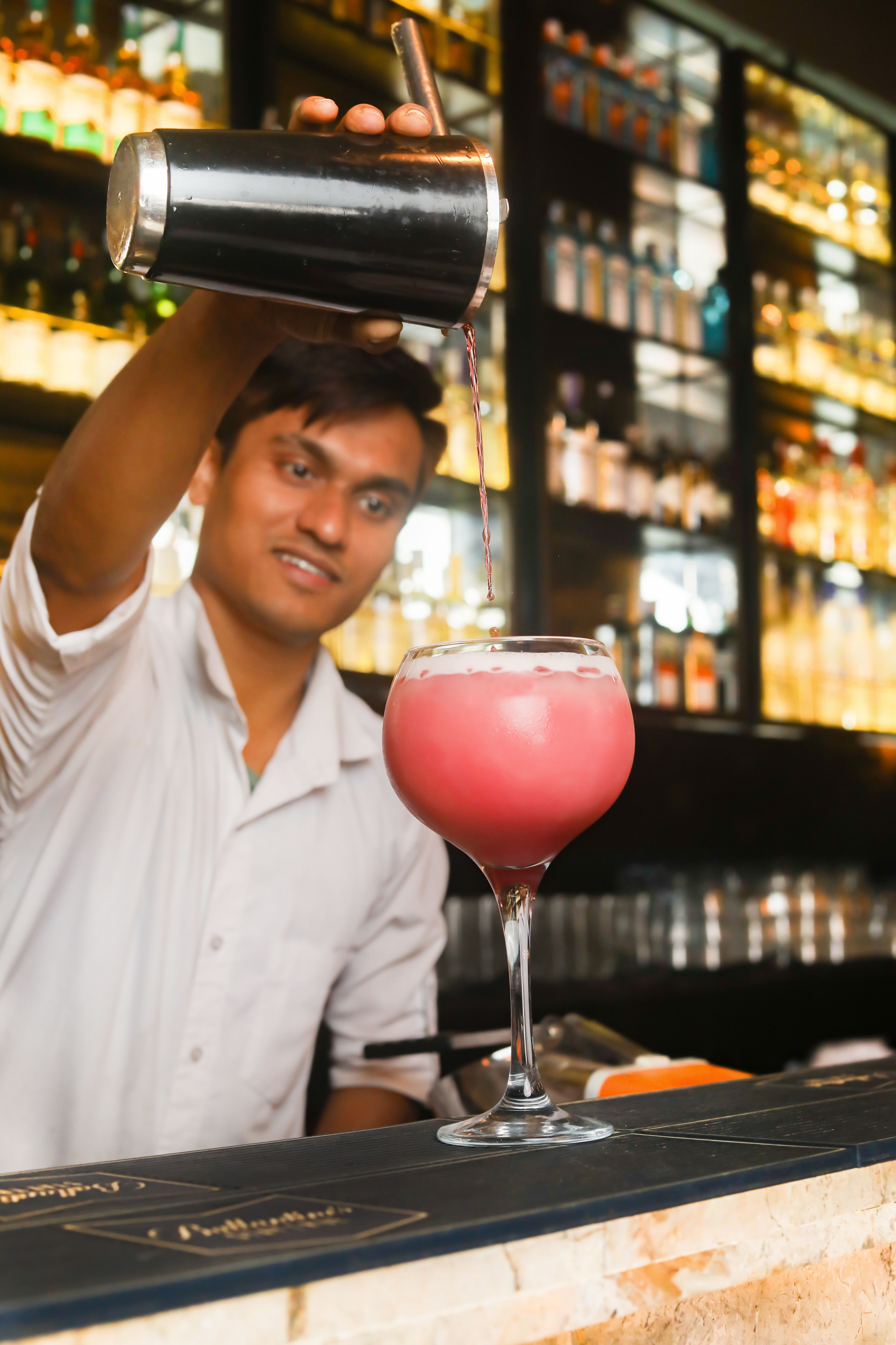 A bartender skillfully prepares a cocktail at a vibrant bar in Bengaluru, India.