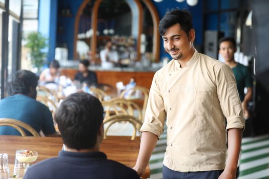 A chef and patron interact in a lively cafe in Bengaluru, India. Warm and inviting atmosphere.
