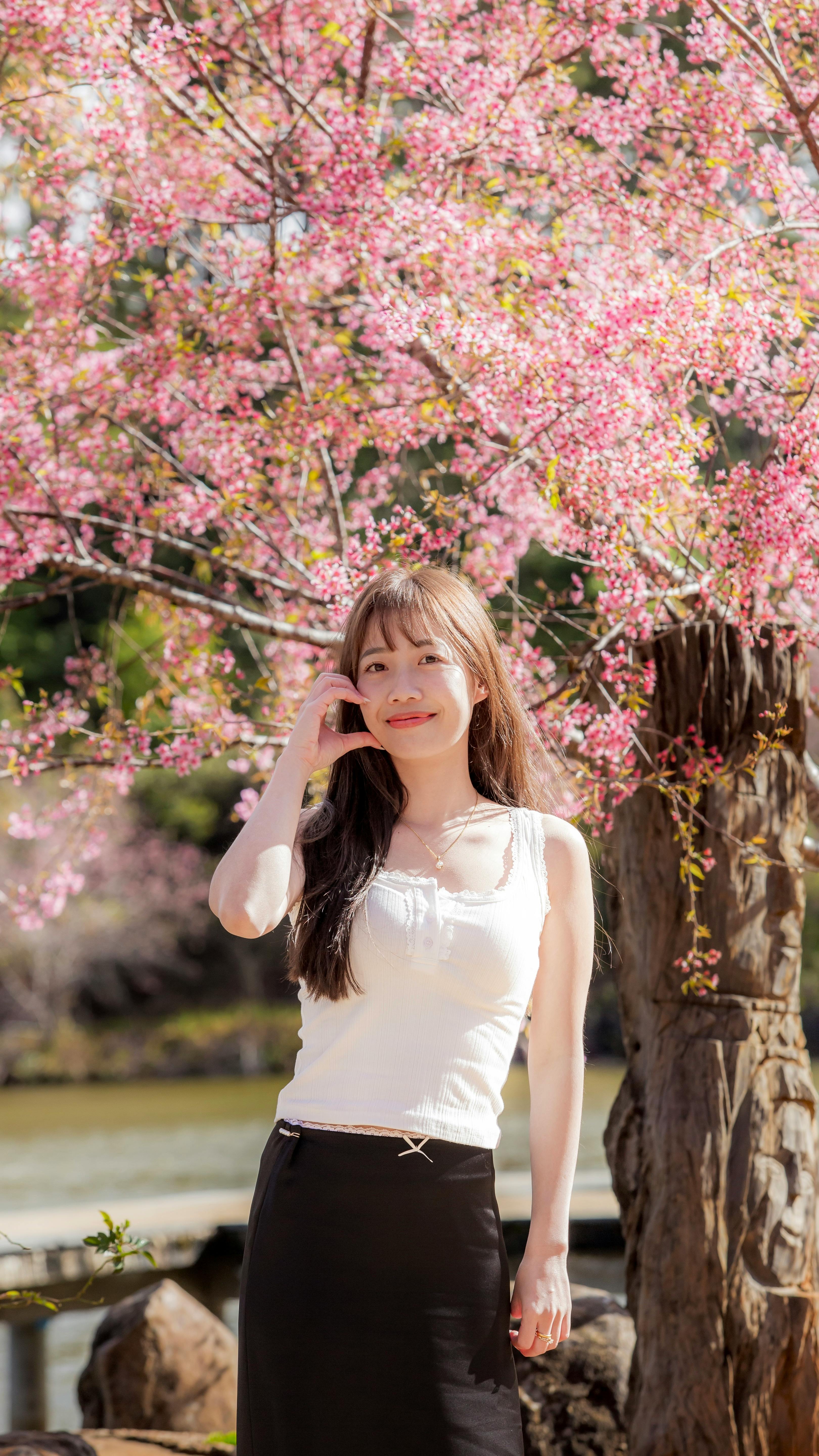 A woman stands joyfully under a blossoming cherry tree, capturing the essence of spring.