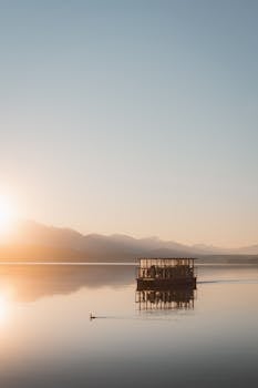 Peaceful sunrise on a tranquil lake with a lone boat reflecting the soft morning light.