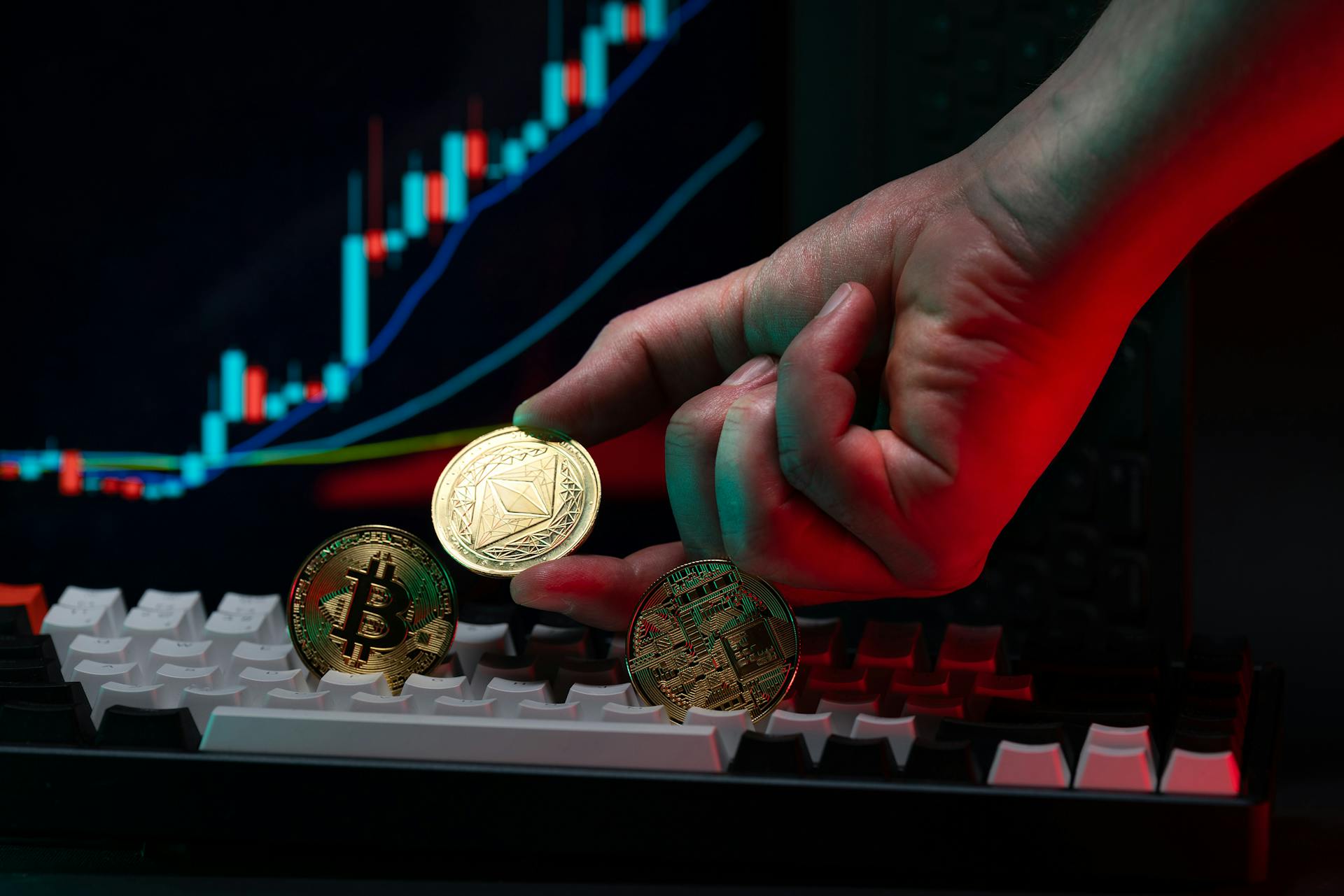 Close-up of a hand holding cryptocurrency coins on keyboard, with a graph display in the background.