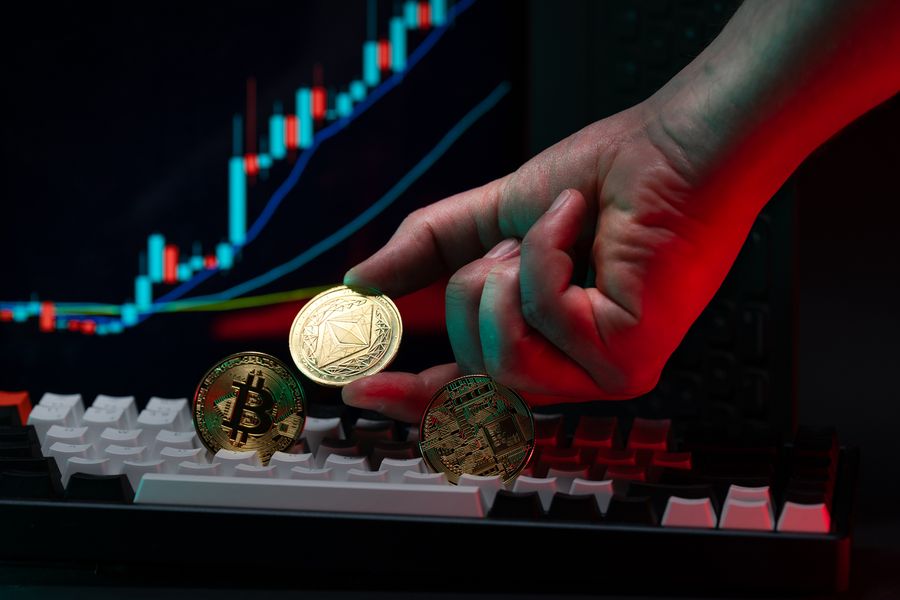A hand holding cryptocurrency coins over a computer keyboard in low light