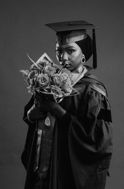 A stylish black and white portrait of a graduate holding flowers.