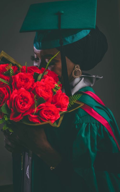 Free A person in graduation attire holds a bouquet of vibrant red roses. Stock Photo