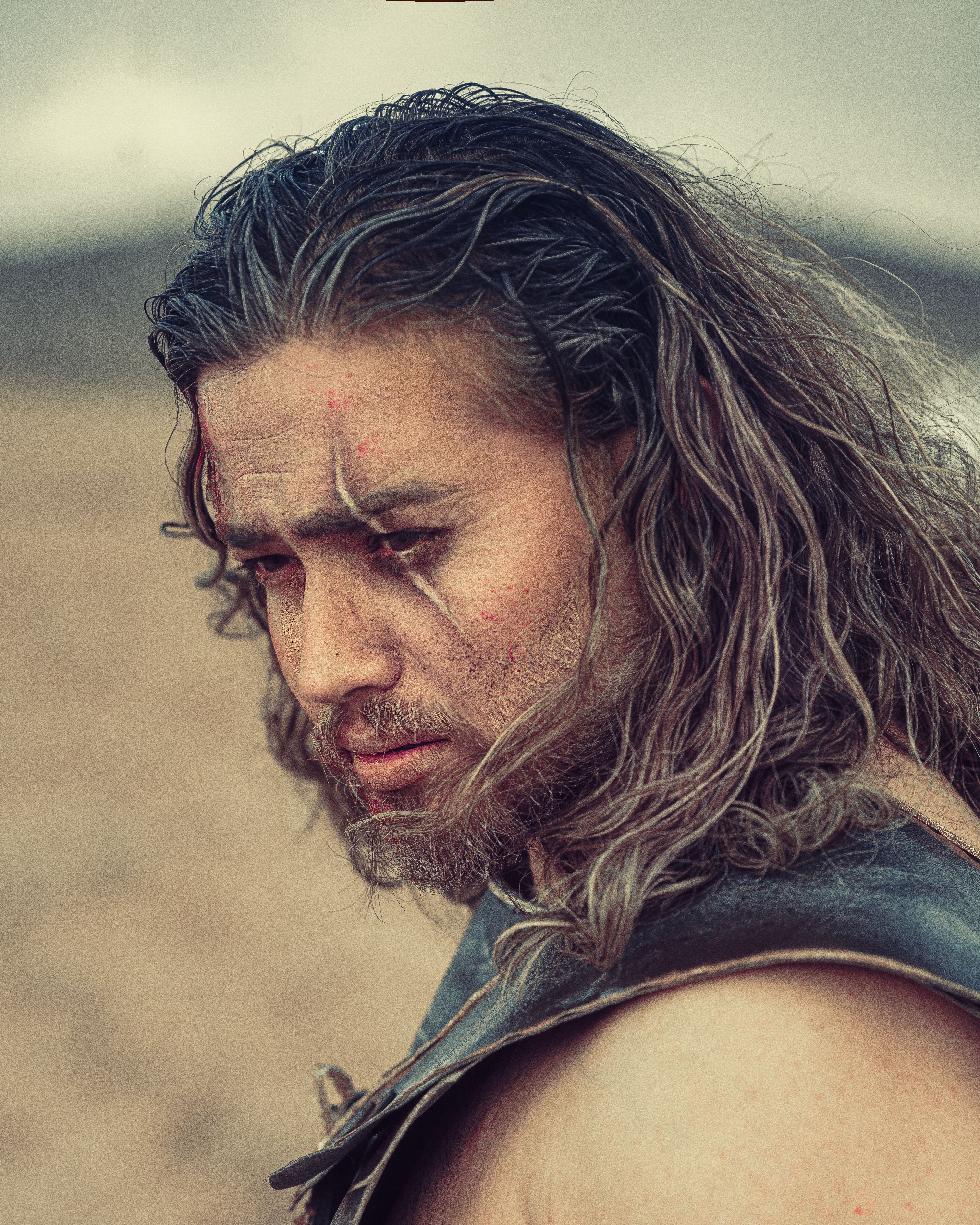A rugged warrior with scars and long hair in a desert landscape, showcasing intense emotion.