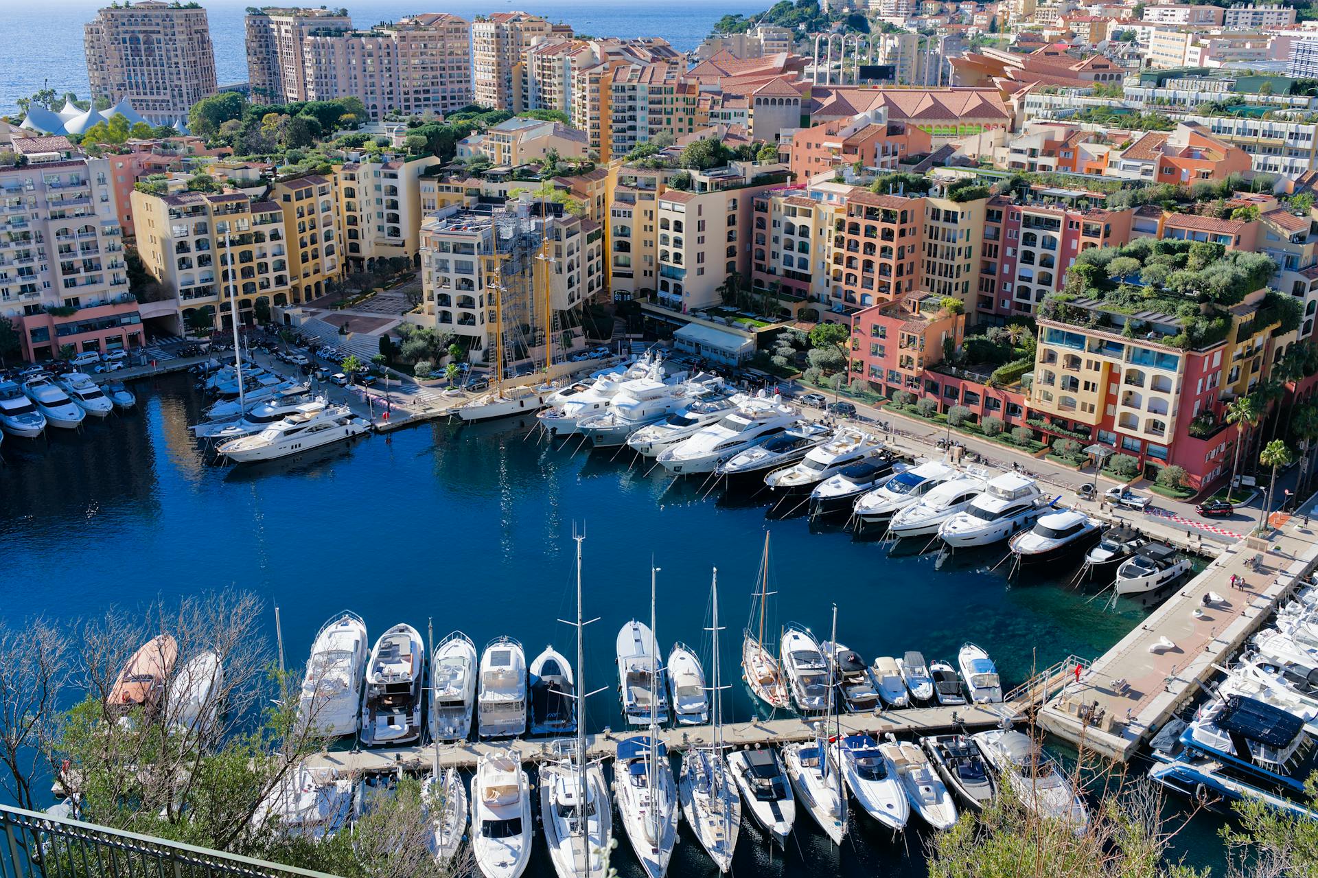 Stunning aerial shot of luxury yachts docked in Monaco's scenic harbor by colorful buildings.