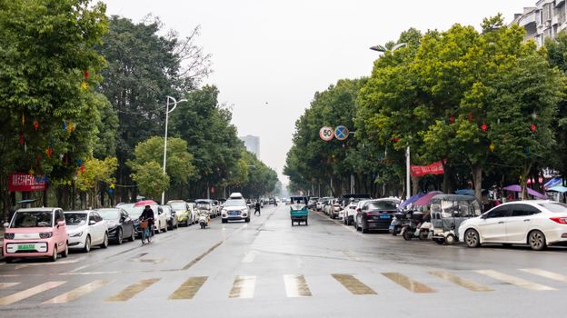 Traffic and pedestrians on a tree-lined street in Guang'an, Sichuan Province, China.