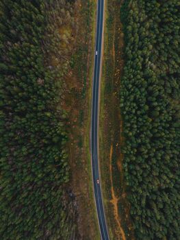 A stunning aerial shot of a road cutting through lush green forest, showing two cars.