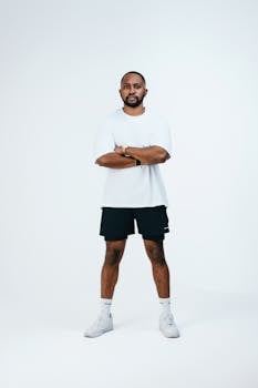 Minimalist studio portrait of a confident man in casual attire, arms crossed, with a clean background.
