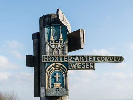 A wooden signpost with intricate carvings highlighting Höxter Abtei Corvey and Weser in Germany.