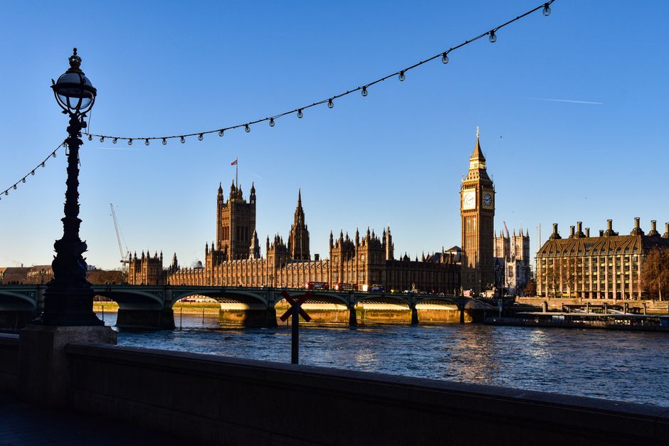 Big Ben and the Houses of Parliament under a clear sky from the Thames banks.